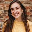 A white woman with long brown hair smiling in front of a brick wall