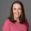 A woman in a pink shirt smiling for a headshot