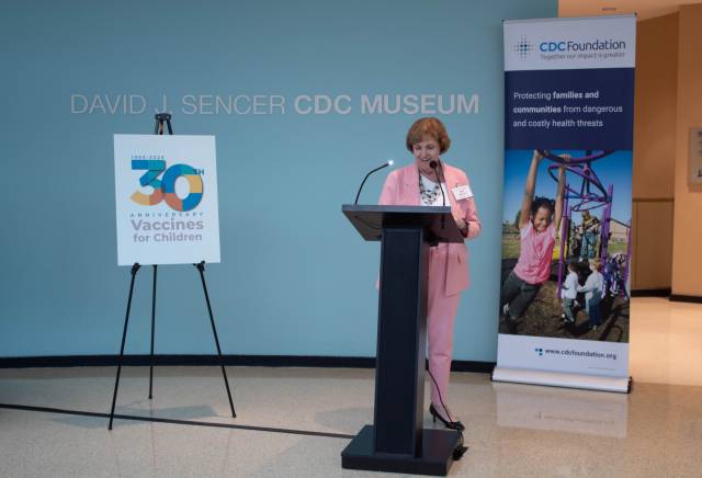 A woman in a pink suit speaks at a podium.