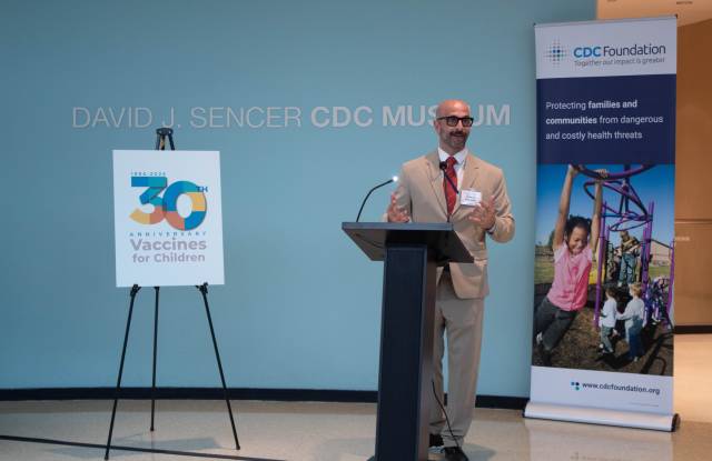 A man in a tan suit talks at a podium.