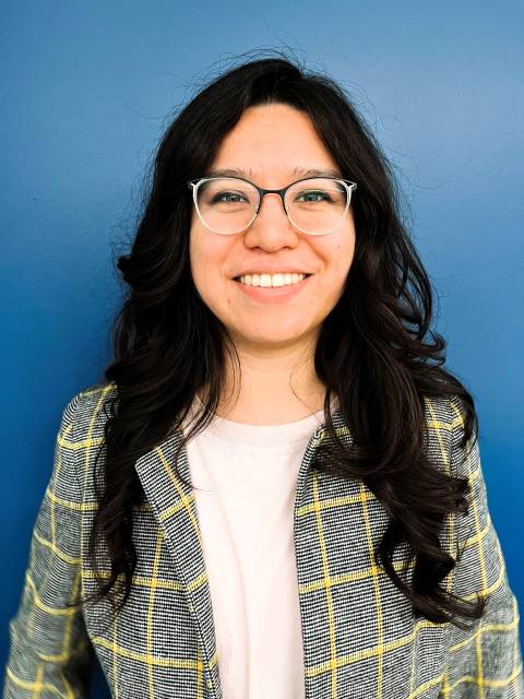 A white woman with long dark hair and glasses smiles