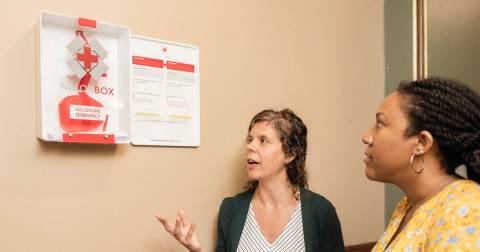 Two women look at a Naloxone box on the wall of a building