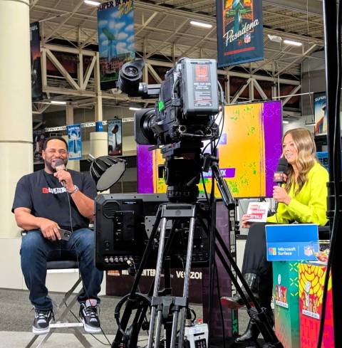 Pro football legend Jerome Bettis holds a microphone, seated in front of a TV camera